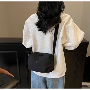 Detailed back view of a compact black nylon crossbody dumpling bag worn by a model