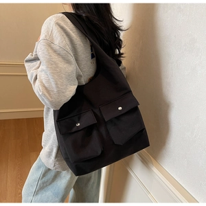 Detailansicht der schwarzen Canvas-Tragetasche mit zwei Vordertaschen und Metallknöpfen