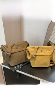 Detail view of nylon crossbody bucket bags in mustard yellow and khaki brown finishes