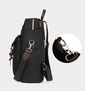 Dettaglio dei ganci in metallo dorato e spalline in pelle marrone su zaino in nylon nero