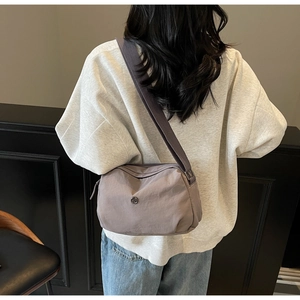 Detail of a casual nylon crossbody bag in smoky purple worn by a model in a minimal setting