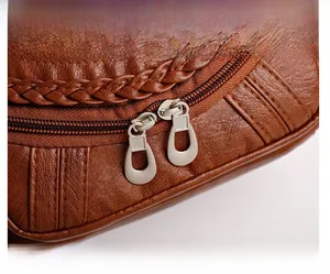 Close-up of premium metal zipper pulls and litchi grain texture on brown leather bag
