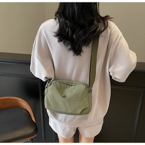 Detail of green dumpling crossbody bag featuring a wide strap and round metal logo
