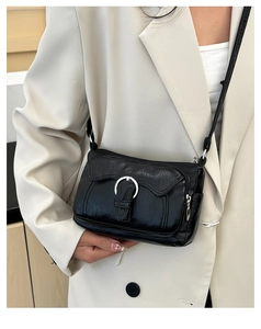 Detailed view of black patent leather shoulder bag with silver buckle on model