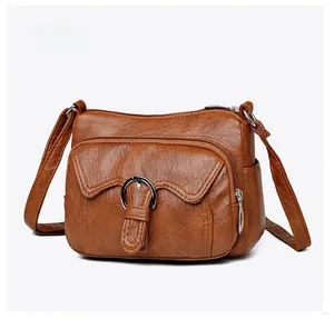 Detailed side view of brown textured crossbody bag with multiple zippers and silver buckles