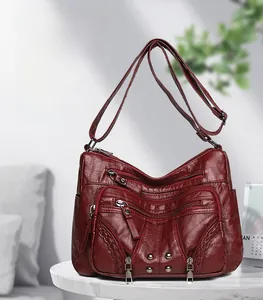 Detail of burgundy leather crossbody bag with zipper pockets and metal rivets on marble
