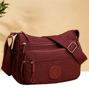 Close-up of waterproof burgundy nylon crossbody bag with multiple zippers and side pocket