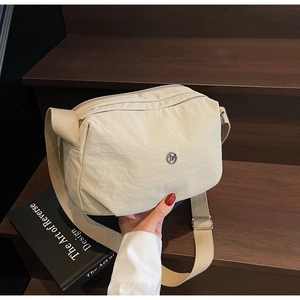 Close-up of beige nylon crossbody bag with adjustable strap on wooden steps