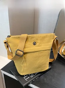 Close-up of a yellow nylon bucket bag with adjustable wide strap and round metal logo