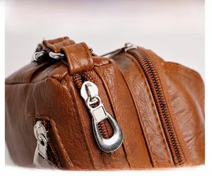 Detail view of brown lychee texture leather shoulder bag with smooth metal zippers