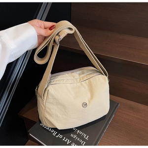 Detail of beige nylon crossbody bag with adjustable strap and metallic logo on books