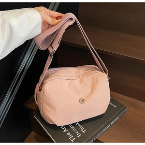 Detail of dusty rose nylon crossbody bag with silver logo on wooden stairs