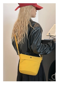Detail view of a bright yellow nylon bucket bag worn by a model in a black leather jacket