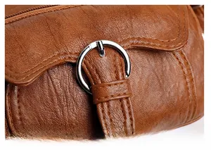 Detailed close-up of silver metal buckle on brown lychee texture leather shoulder bag