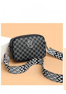Détail du sac caméra en cuir noir avec motif M et bandoulière large élégante