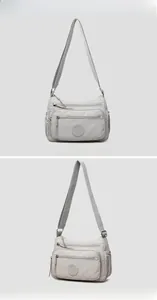 Detail of light gray nylon crossbody bag showing multiple zip pockets and adjustable strap