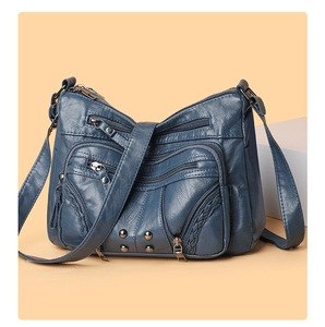 Detail of dark blue faux leather crossbody bag with multiple zippers and metal rivets