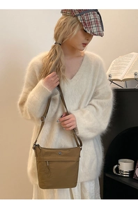 Brown nylon crossbody bucket bag with multiple zippers shown in a cozy lifestyle setting