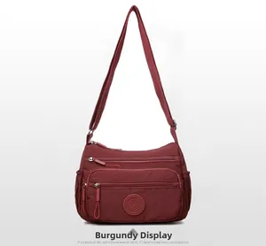 Detail of wine red nylon crossbody bag showing multiple zippers and adjustable strap