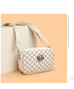 Détail d'un sac caméra crème avec motif monogramme et large bandoulière en tissu