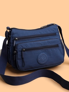 Detail of dark blue waterproof nylon crossbody bag showing multiple functional zipper pockets