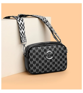 Détail du sac caméra noir avec motif M et large bandoulière zigzag sur un support