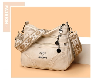 Detail of beige shoulder bag featuring multi-layer zippers and embroidered floral strap