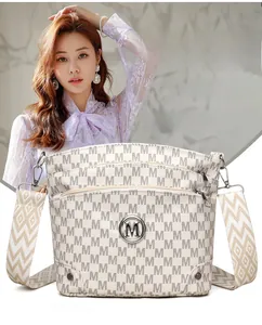 Detail view of cream shoulder bag with M-pattern print and woven geometric strap