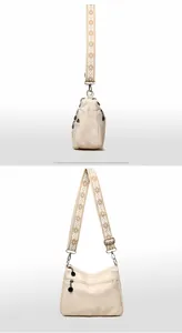Detail view of beige canvas tote bag showing embroidered strap and multi-zipper pockets