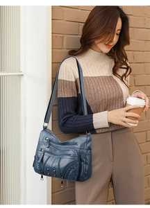 Detail of dark blue soft leather crossbody bag with multiple zip compartments and rivets