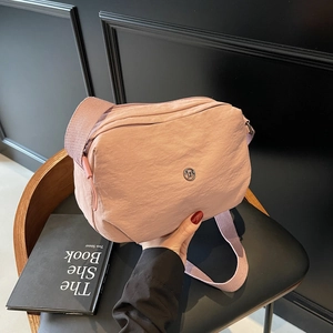 Pink nylon dumpling bag with adjustable shoulder strap and metal logo on black background