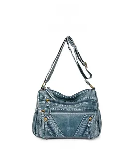 Detailed front view of blue denim texture crossbody bag with multiple brass zipper compartments