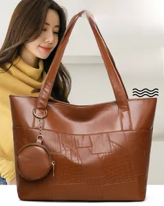 Dettaglio della borsa tote in pelle marrone con cuciture a coccodrillo e ciondolo portamonete