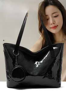 Detail of a black glossy tote bag with white TOTE BAG text and a round coin purse charm