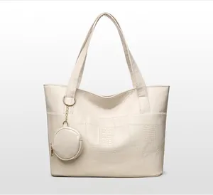 Dettaglio della borsa tote bianco sporco con trama coccodrillo e ciondolo portamonete tondo
