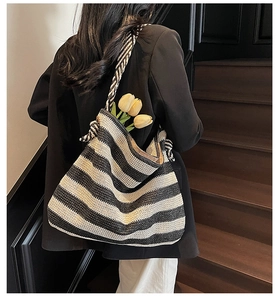 Detail of striped woven straw beach tote with knotted shoulder strap and floral decor