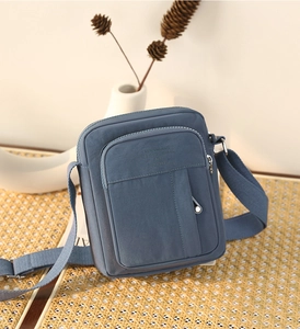 Close-up of blue canvas crossbody bag with multi-zipper pockets and embossed text detail