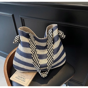 Detail of blue and white striped straw beach bag with knotted handle on a black chair