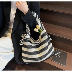 Close-up of a woven straw beach bag featuring black and white stripes and a knotted handle