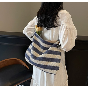 Blue and white striped straw beach tote bag shown on model with floral white dress