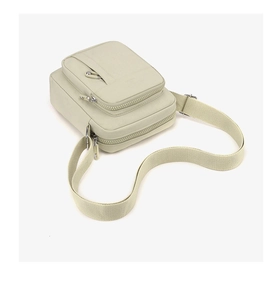 Detail view of cream beige canvas crossbody bag with multi-layer zippers and soft texture