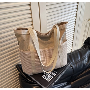 Detalle de bolso tote de nailon beige con bolsillos de malla en un sofá de cuero