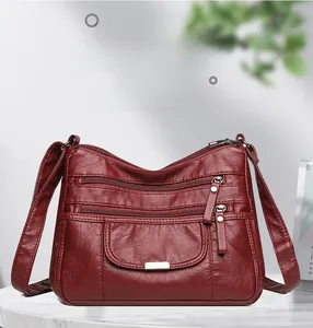 Detail view of dark red multi-layer soft leather shoulder bag with functional zippers