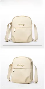 Detail of a beige nylon crossbody mobile phone bag with golden metal logo and zippers