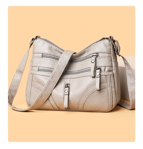 Close-up of soft faux leather crossbody bag with multiple front zipper pockets in light grey
