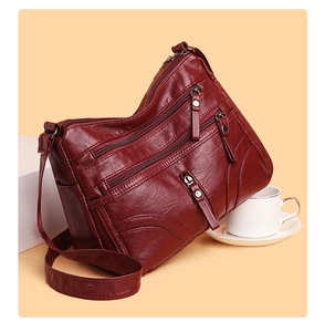 Detail view of wine red crossbody bag featuring three layered zippered pockets and lychee texture