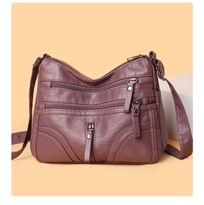 Detail view of a soft dark purple leather crossbody bag with multiple zip pockets