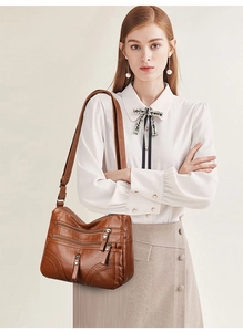 Close-up of brown soft leather crossbody bag with multiple functional zippers and wide strap