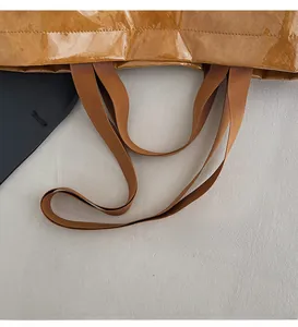 Close-up of brown tote bag showing glossy textured fabric and long braided shoulder straps