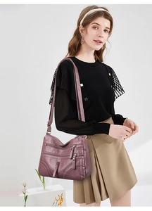 Detail of mauve soft leather crossbody bag with multiple zipper pockets on model